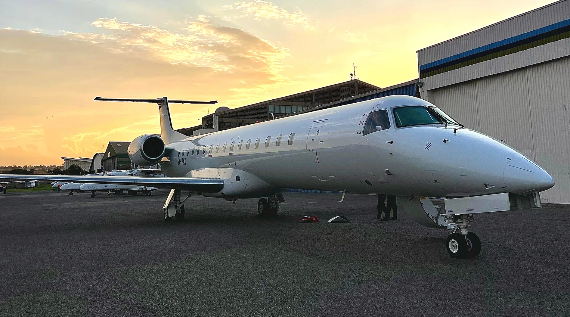 An ALS Embraer ERJ-145 outside the hangar under a low sun